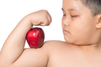 A child flexes his arm muscle with a big red apple balanced upon it