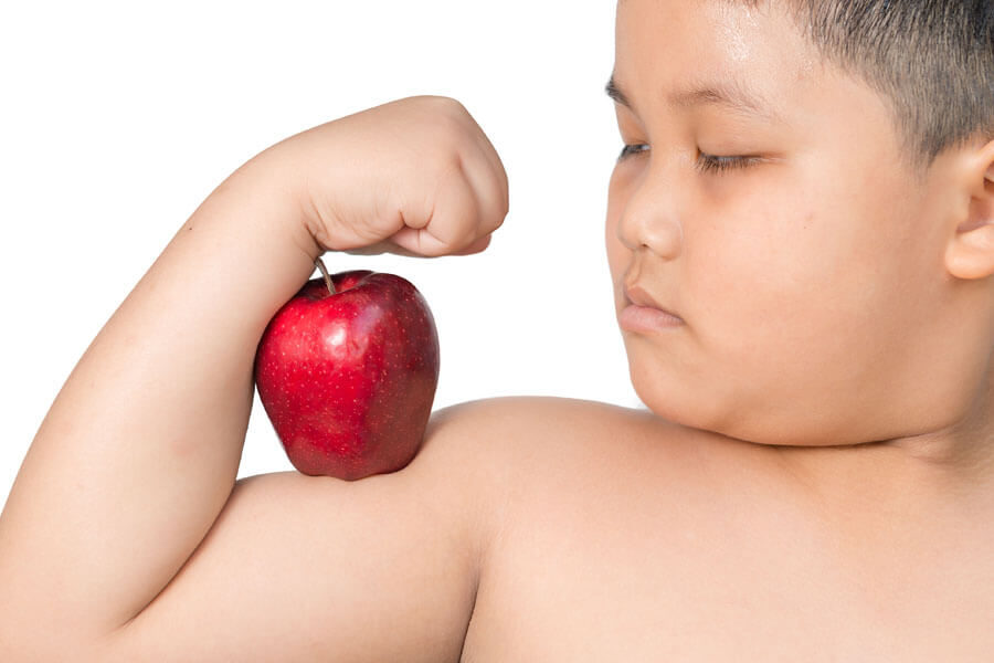 A child flexes his arm muscle with a big red apple balanced upon it