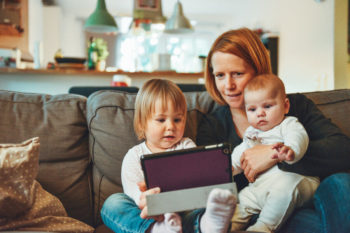 A mother and small children on a sofa look at a tablet together