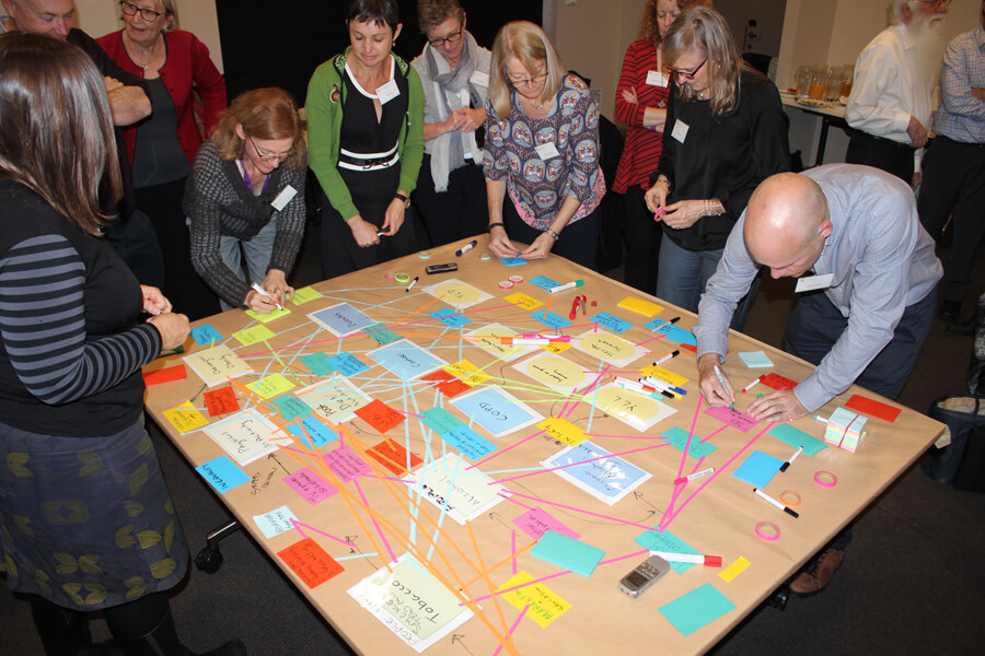 Policy makers and academics at a workshop in Canberra group around a table, arranging the coloured papers on it as part of a modelling exercise.
