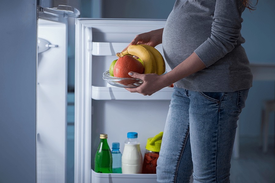 Pregnant woman pulling healthy food from a fridge