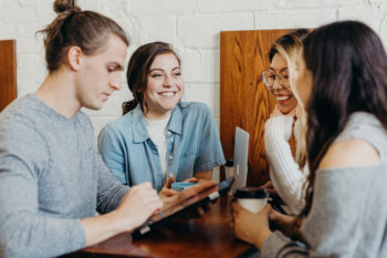 A group of young people chat and use their devices over a coffee