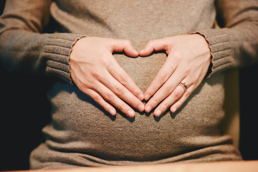 A pregnant woman makes a heart shape with her hands across her tummy.