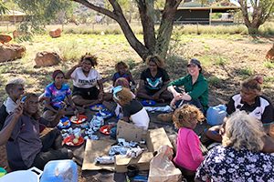 A group of elders and young people seated in the shade of a tree at a bush picnic in the APY Lands