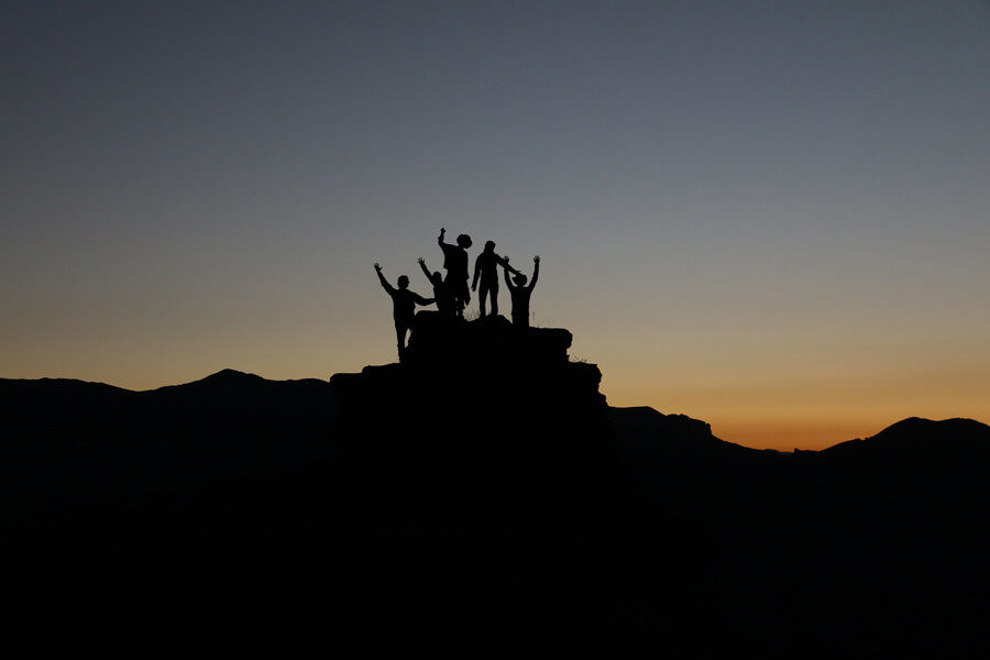 A group of people celebrate reaching a mountain summit at sunset