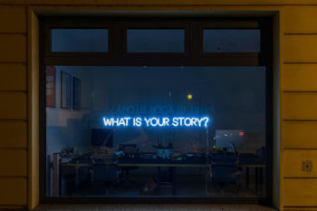 A neon sign reads: What is your story?