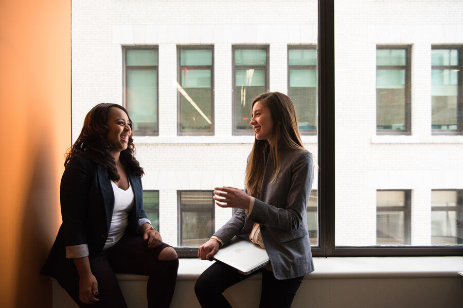 Colleagues in a workplace laugh as they chat by a window