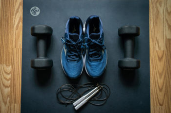 Dumbbells, skipping rope and running shoes on a yoga mat