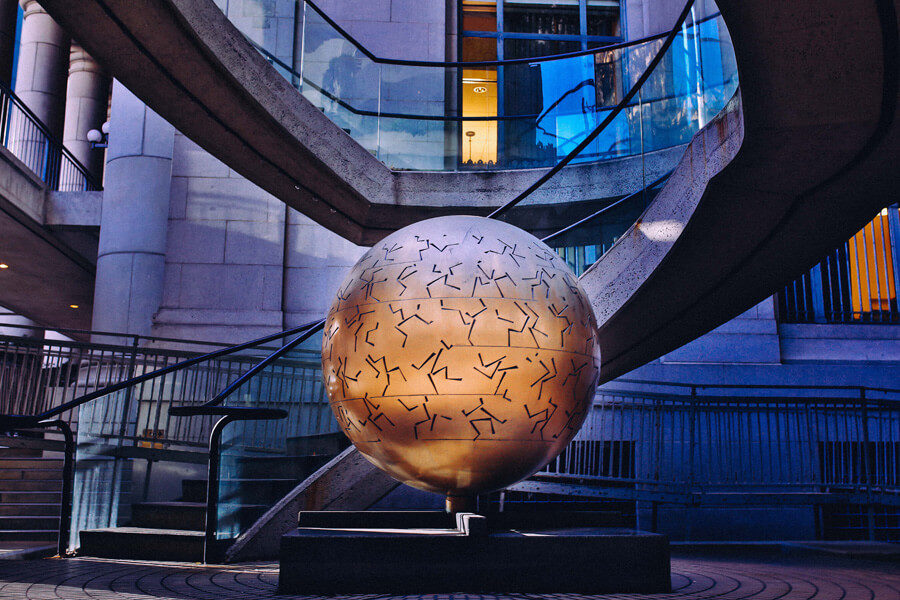 A large public sculpture of a metal globe covered in rings of stick figures sits in the well of an exterior circular staircase
