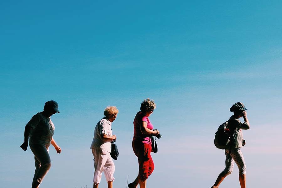 Older people walking against a clear blue sky, carrying cameras and backpacks