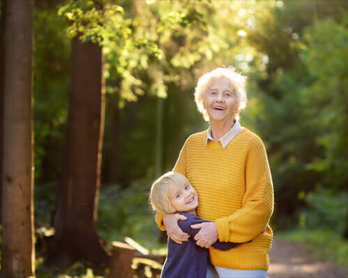 A happy grandmother and grandchild share a warm embrace on a forest path as the sun shines
