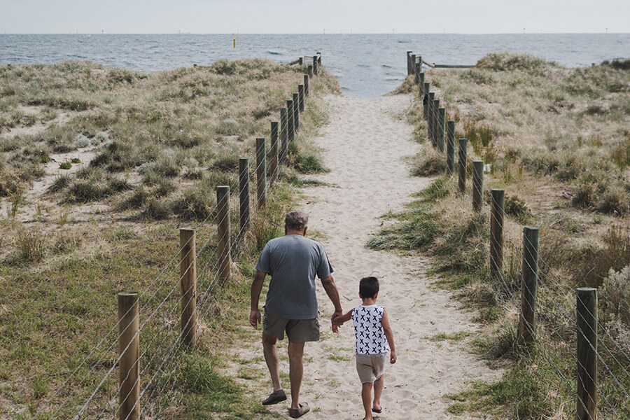 Grandfather and grandson going along a sandy path to the beach near Melbourne, Australia. Photo by Johan Mouchet on Unsplash
