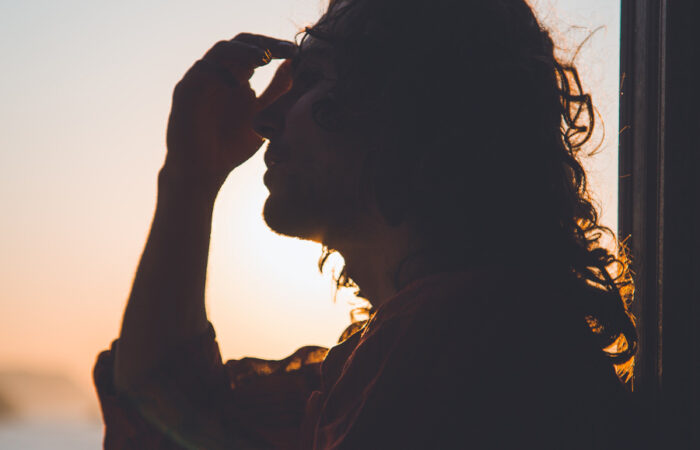 Man clutching his head as the sun sets behind him. Photo by Matteo Vistocco on Unsplash