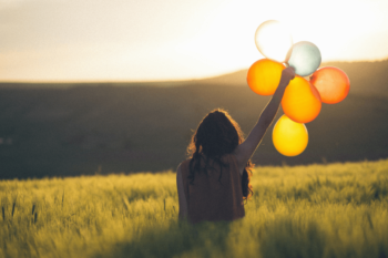 Woman holding balloons in a field at sunset