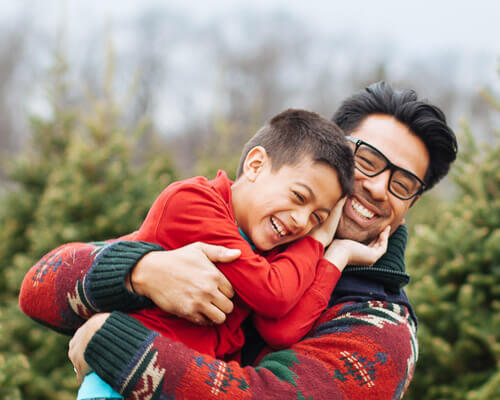 A father and son in Christmas jumpers embrace warmly by a forest of Christmas trees. Image by Joseph Gonzalez on Unsplash, reference NCR1FHsrl3U