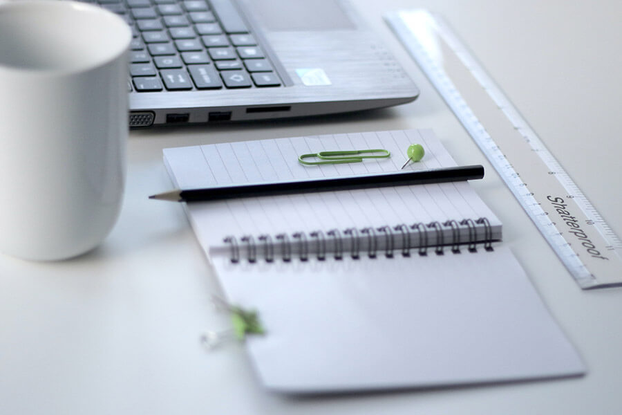 A desk with pen and paper, laptop and mug. Photo by Oli Dale on Unsplash