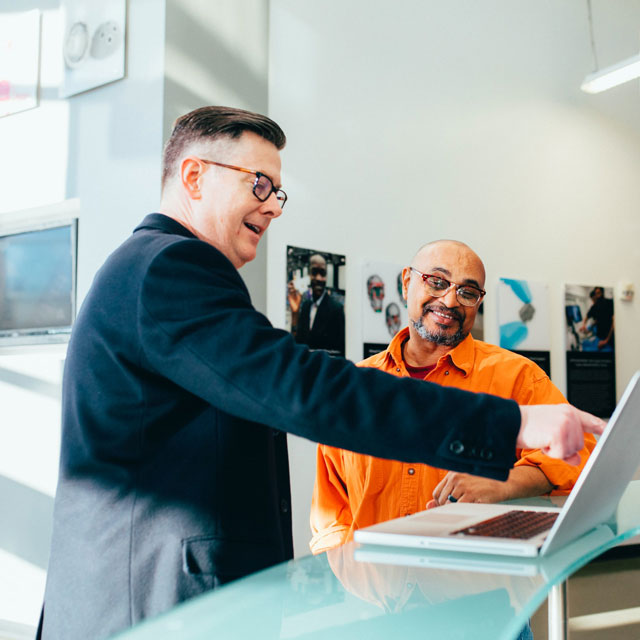 Two people smile as they discuss something on their laptop