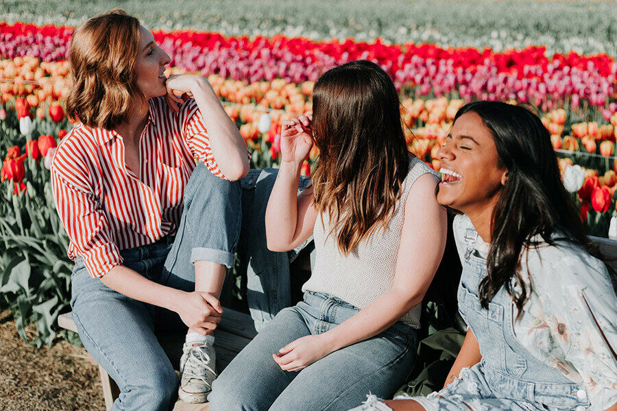 Three friends share a moment together on a bench beside a flower bed. Image by Priscilla du Preez on Unsplash