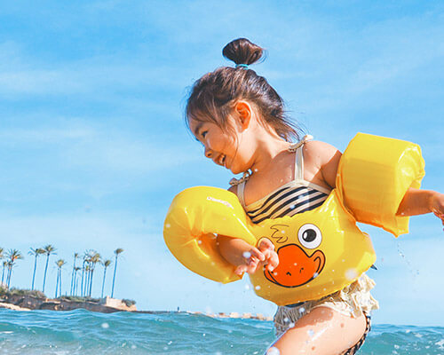 A child wearing floatation devices excitedly plays in shallow ocean water. Image by Leo Rivas on Unsplash.