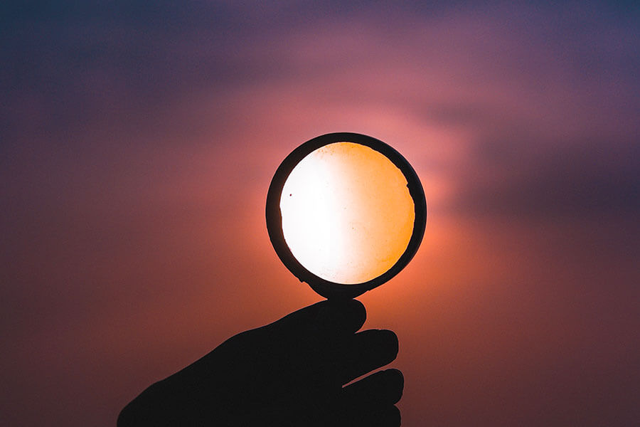 A hand holds a magnifying glass up to a beautiful sky at sunset. Image by ahmed zayan on Unsplash