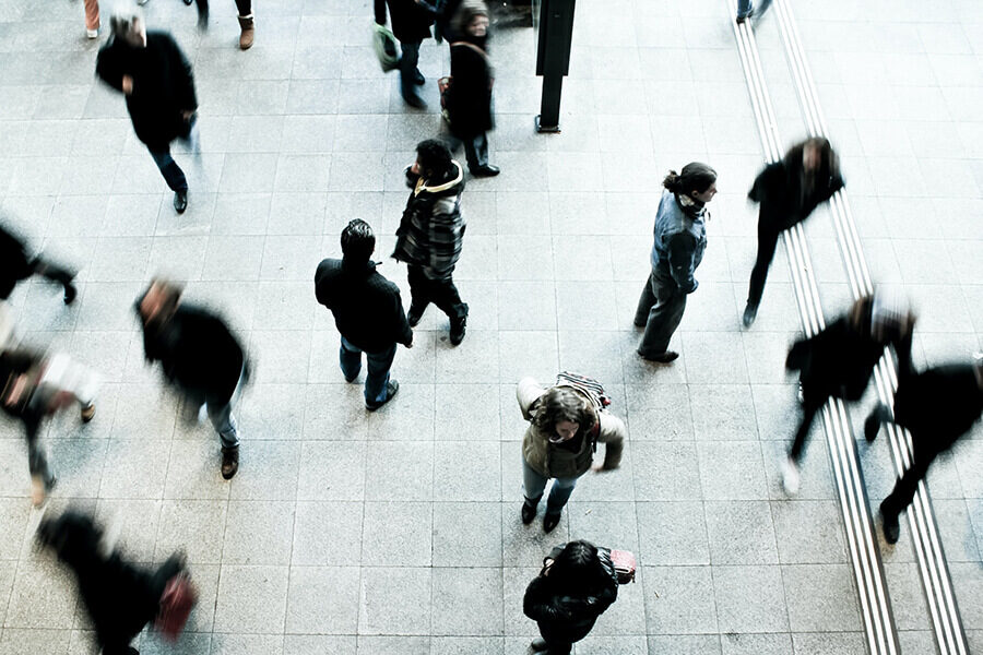 People walk through a busy public thoroughfare as one person stands still. Photo by timon studler on Unsplash.