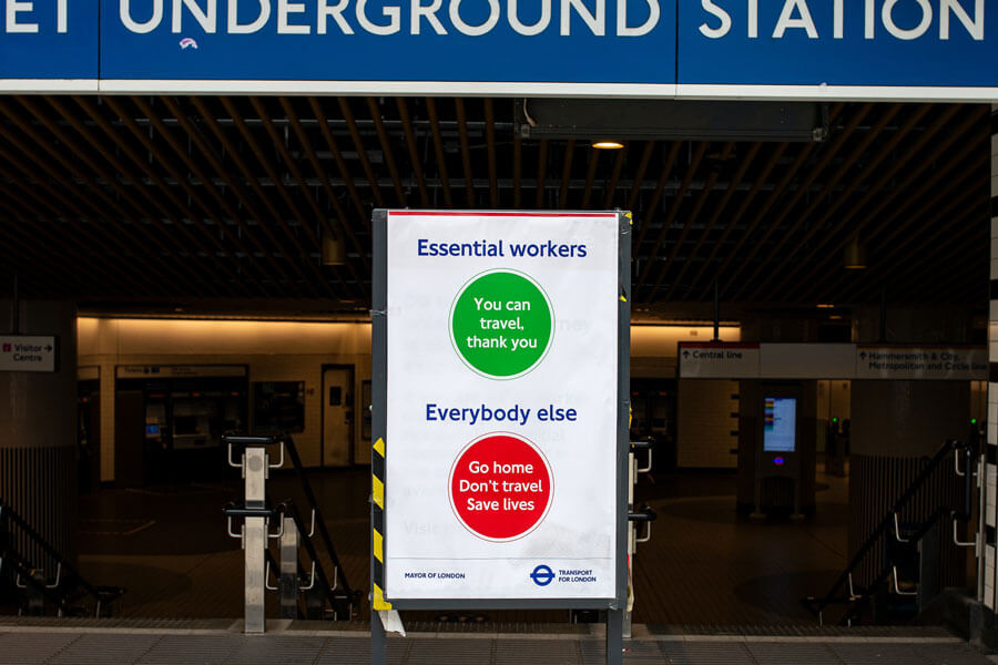 A London Underground station entrance during the COVID-19 pandemic. The station is open, but a sign outside reads in green: "Essential workers: You can travel, thank you", and in red: "Everybody else: Go home. Don't travel. Save lives." Image by Ben Garratt on Unsplash.