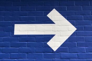 A blue wall painted with a huge white arrow. Image by nick fewings on Unsplash.