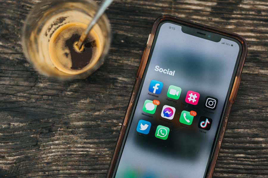 A phone showing various social media apps rests on a table with a cup of coffee. Image by nathan dumlao on Unsplash
