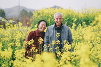 Smiling older couple, man and woman, in a field of yellow flowers